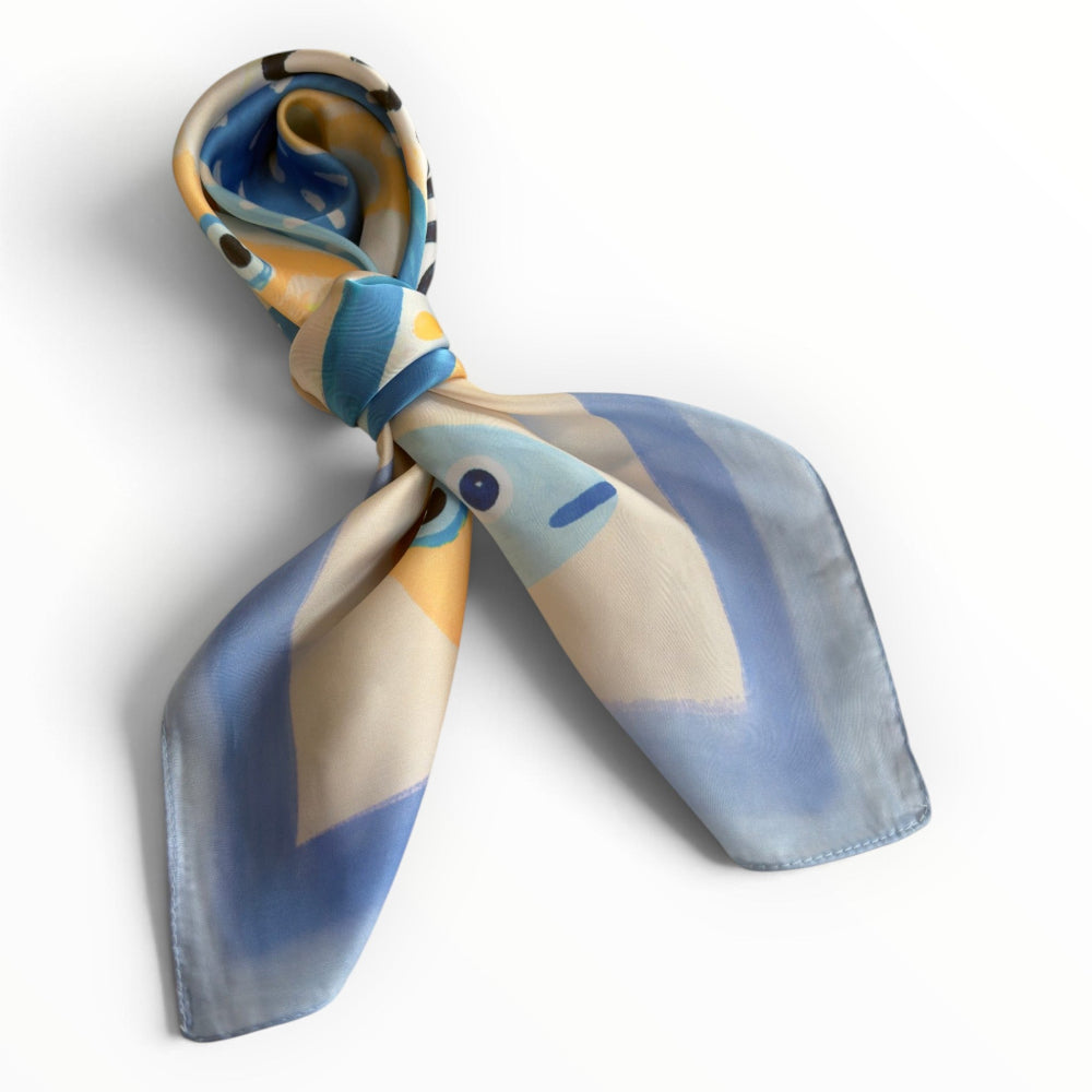 Sardine Chic blue fish-print silky square scarf tied in a stylish neckerchief knot, showing its playful coastal design.