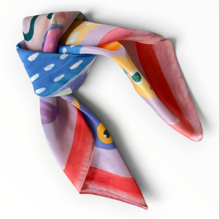 Pink sardine-print square scarf styled in a decorative knot, featuring coral-pink edges, lavender and bright blue fish illustrations.